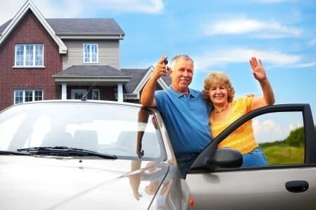 Happy couple holding keys beside their delivered car in their driveway