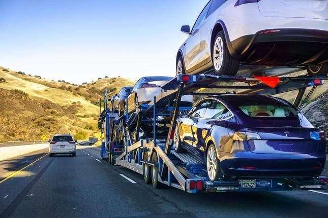 Open car carrier loaded with sedans on a golden-hills interstate highway